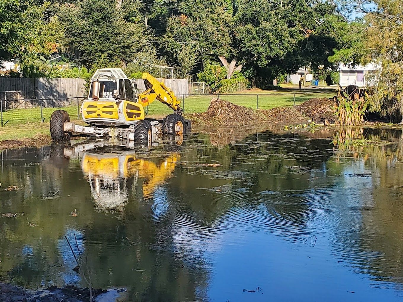 A yellow excavator is cleaning a pond in a park.