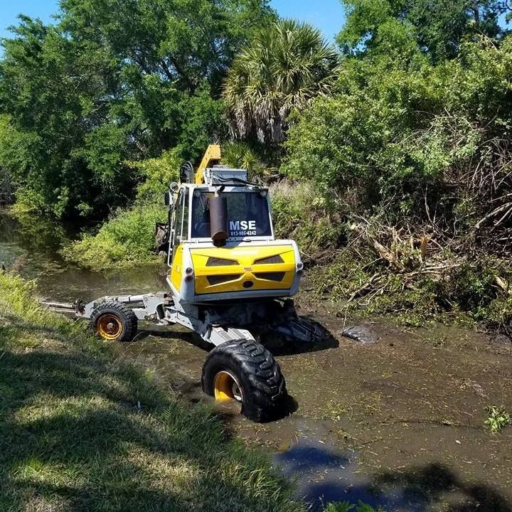 A yellow and white excavator is driving through a swamp.