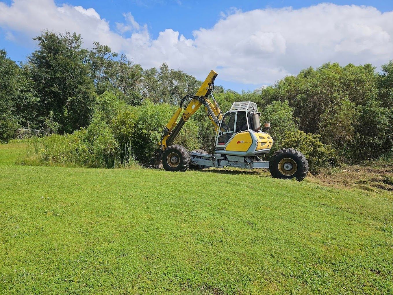 A yellow and white tractor is driving through a grassy field.