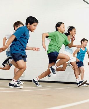 A group of children in gym attire running across an indoor court.