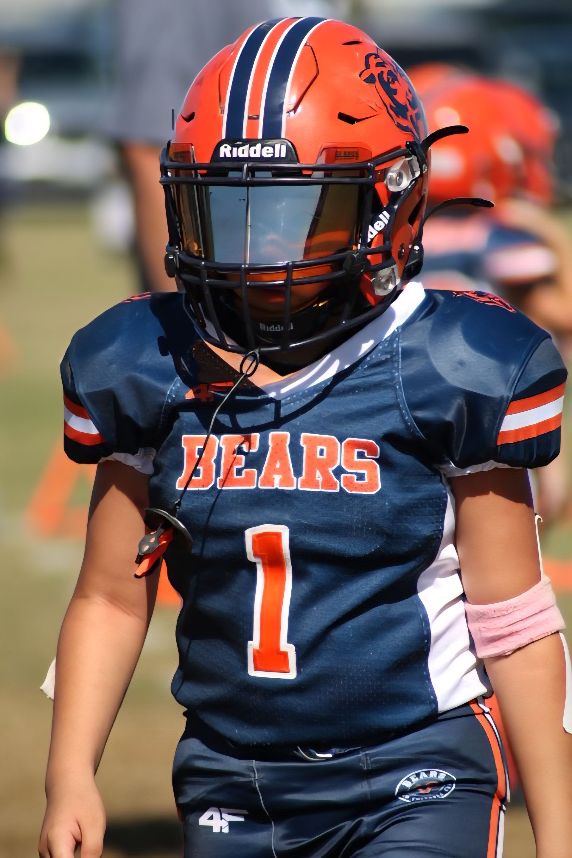 A football player in a blue and orange jersey with the number 1 and a matching helmet with a dark visor stands on a field.