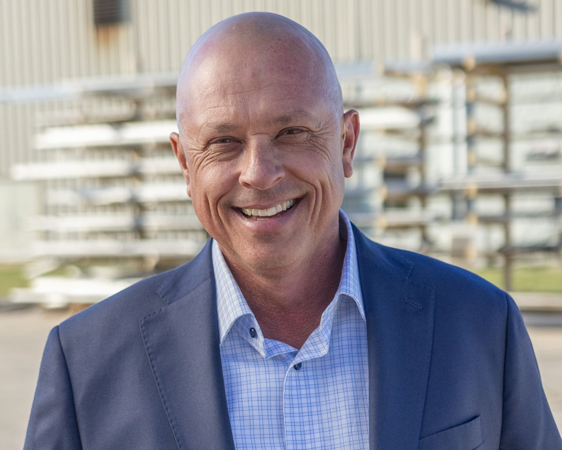 Smiling man with a shaved head in a blue plaid blazer and blue button-down shirt.
