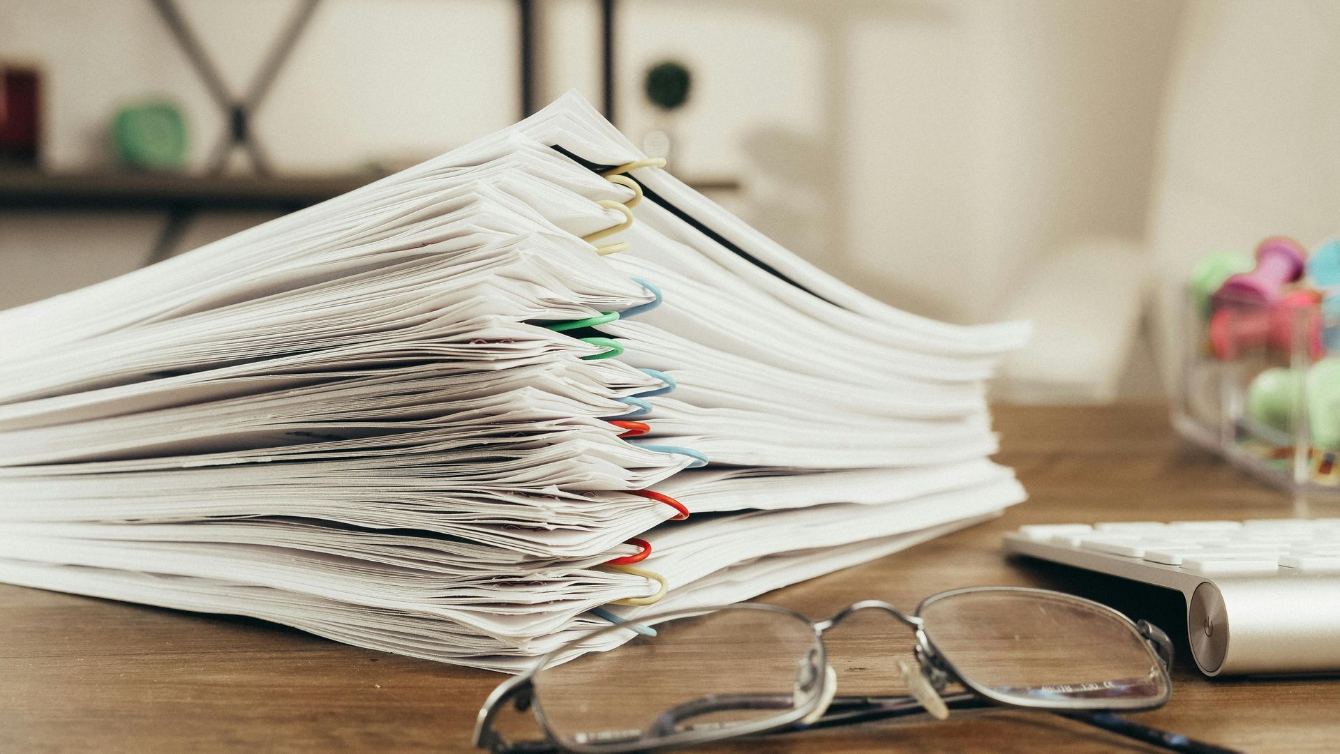 Stack of papers with colored tabs beside eyeglasses on a wooden desk