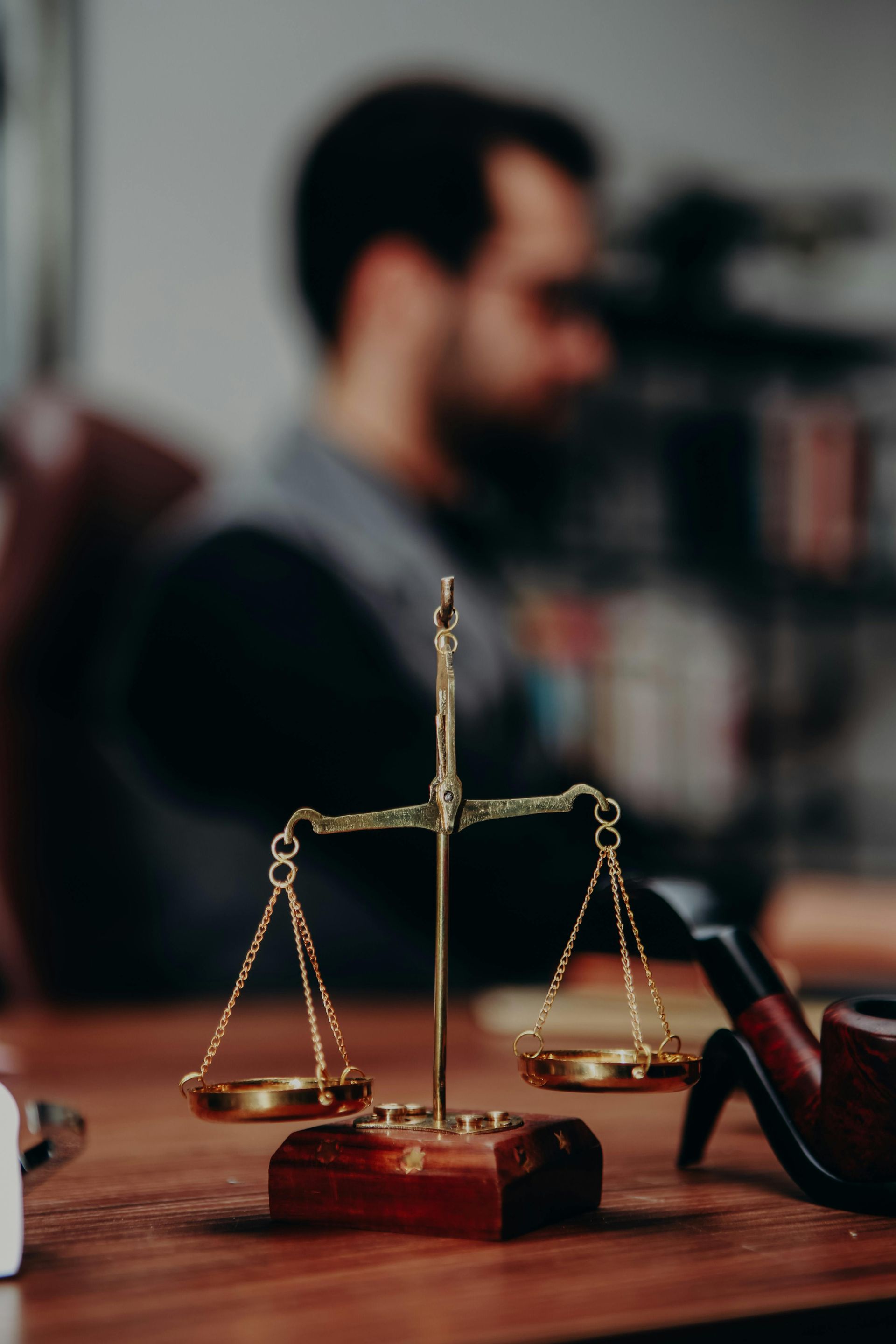 Golden justice scales on a wooden desk, with a blurred person and law office in the background