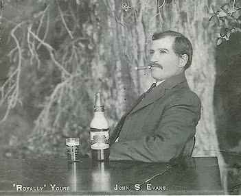 A man in a suit is sitting at a table with a bottle of beer and a glass of beer.