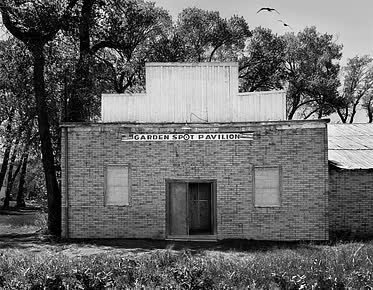 A black and white photo of an old brick building with trees in the background.