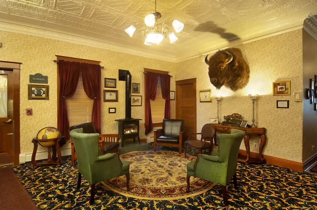 A living room with green chairs and a buffalo head on the wall.