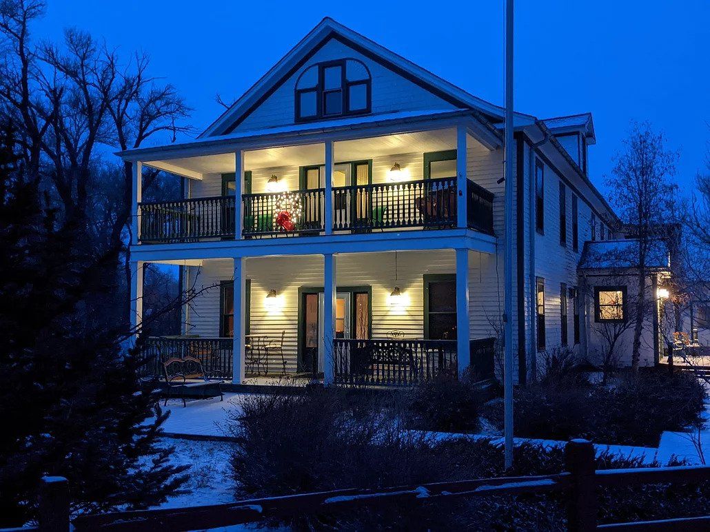 A large white house with a large porch is lit up at night.