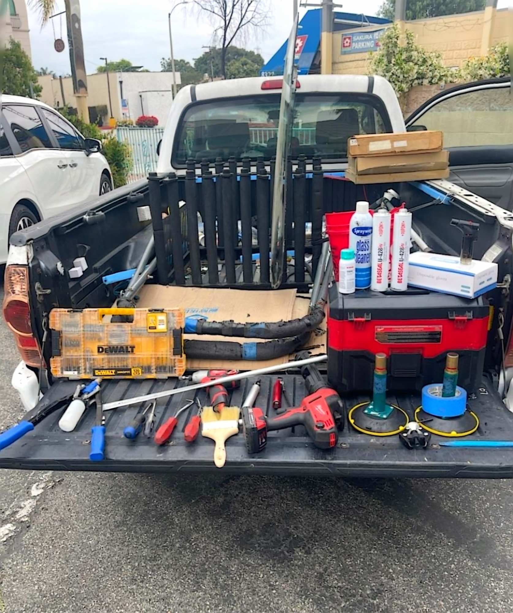 A pickup truck bed holds various tools, including a drill, brushes, a tool case, and construction supplies.