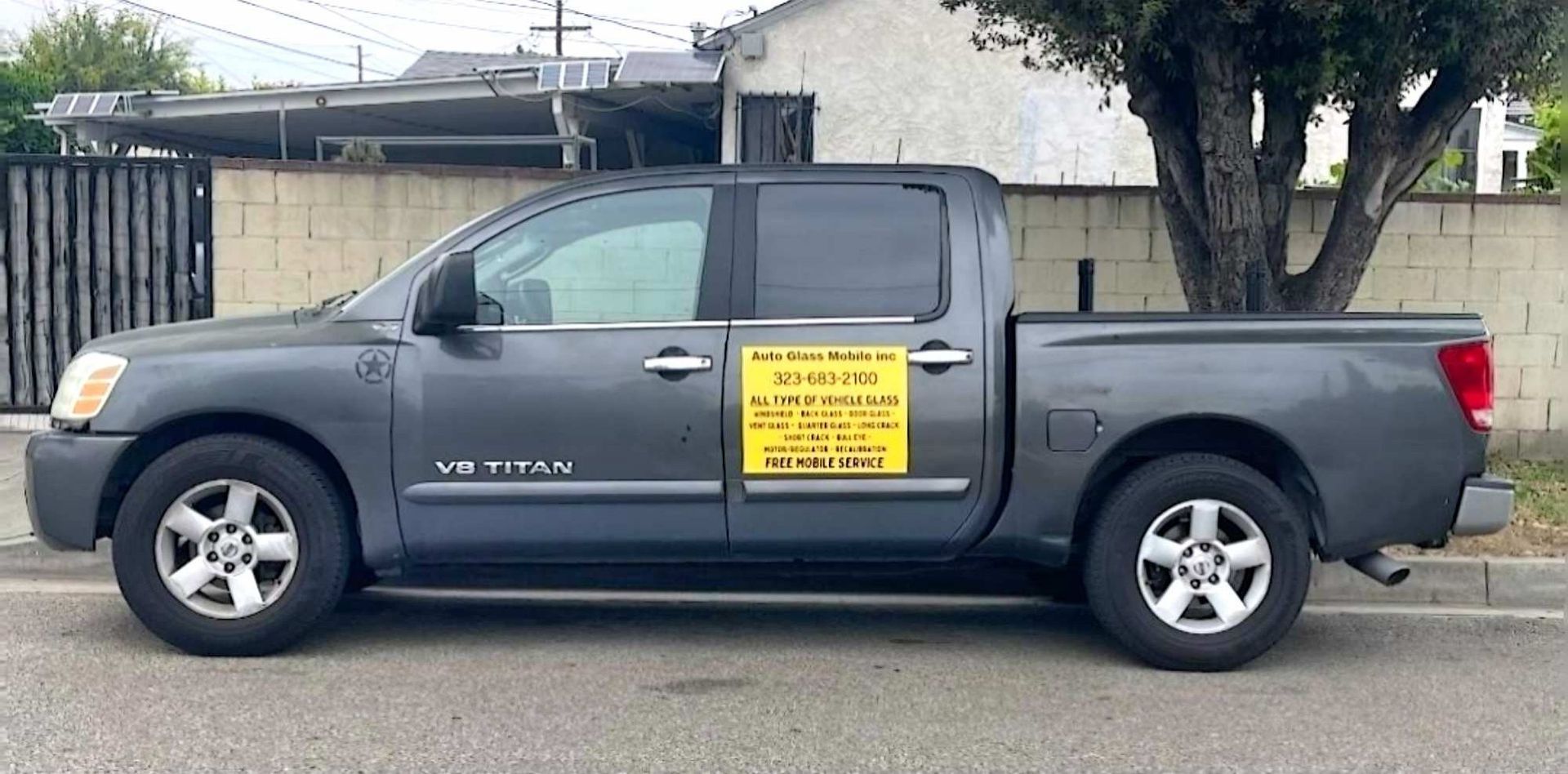 A dark gray Nissan Titan pickup truck parked on the street with a yellow business advertisement sign on the driver door.