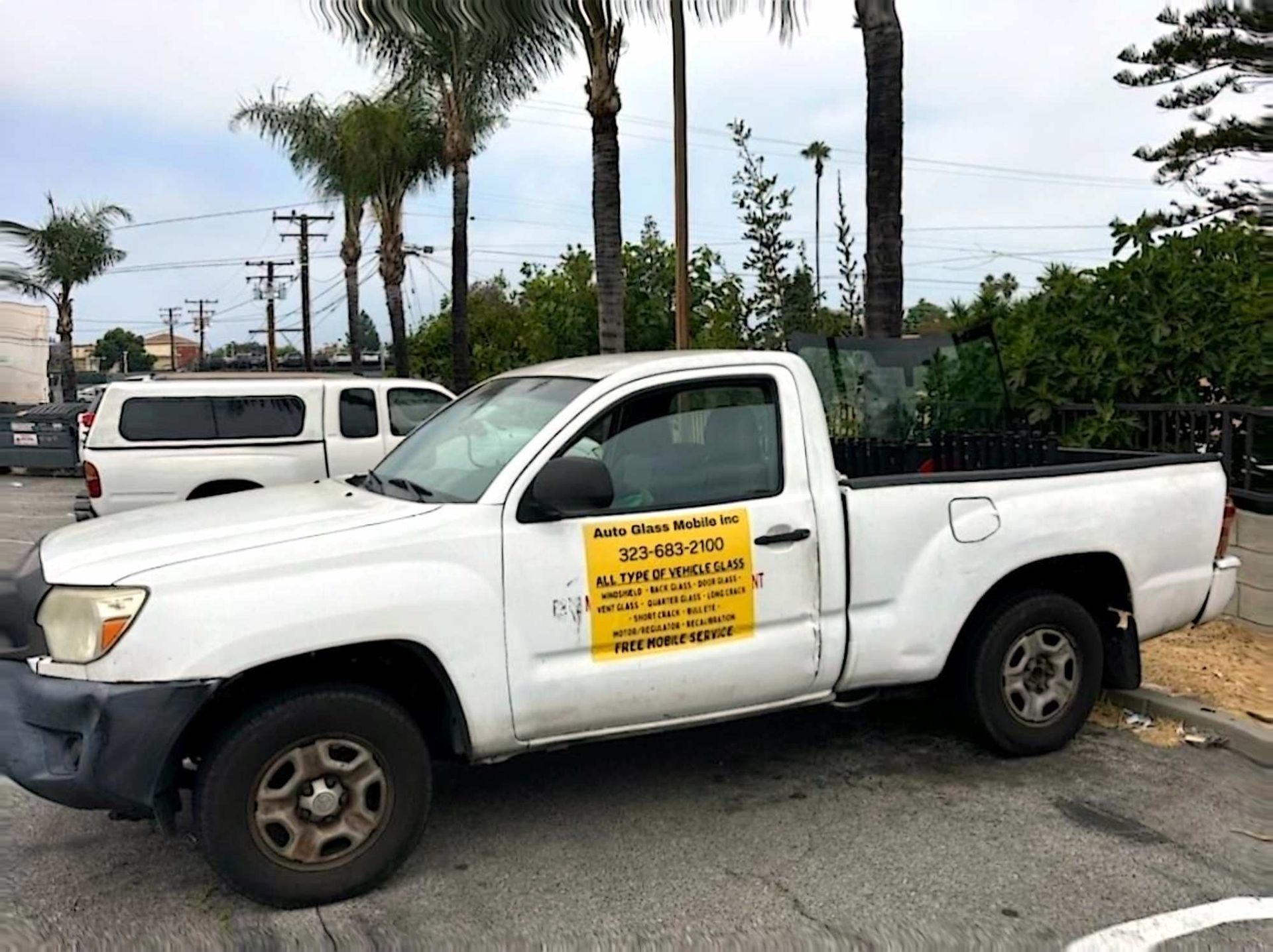 A white pickup truck parked outdoors, featuring a yellow sign on the driver's door with business information.