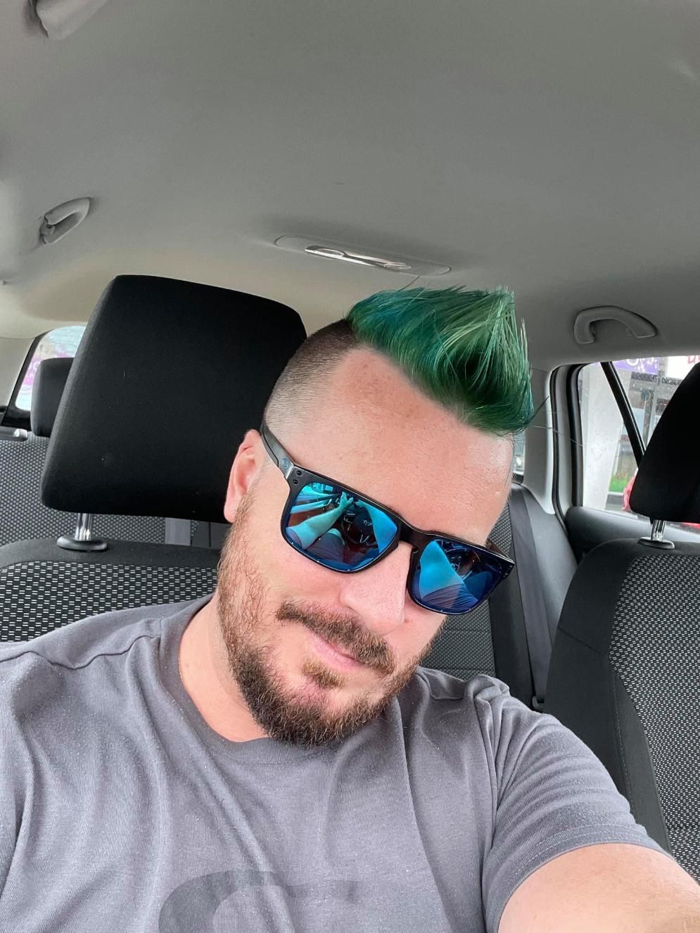 A Man With Green Hair And Sunglasses Is Sitting In A Car — Klic's Hair Design In Earlville, QLD