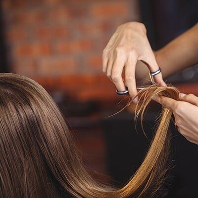 A Woman Is Getting Her Hair Cut By A Hairdresser At A Salon — Klic's Hair Design In Earlville, QLD
