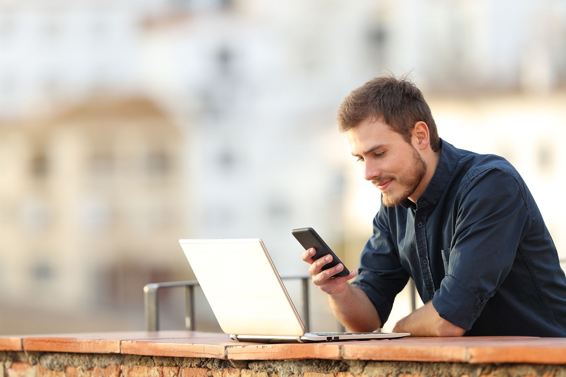 A man is sitting at a table with a laptop and cell phone