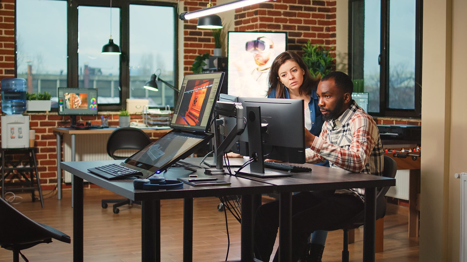 A man and a woman are sitting at a desk looking at a computer screen.