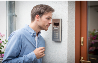 Man using a door intercom. He is looking at the screen, and the wall and door are visible.