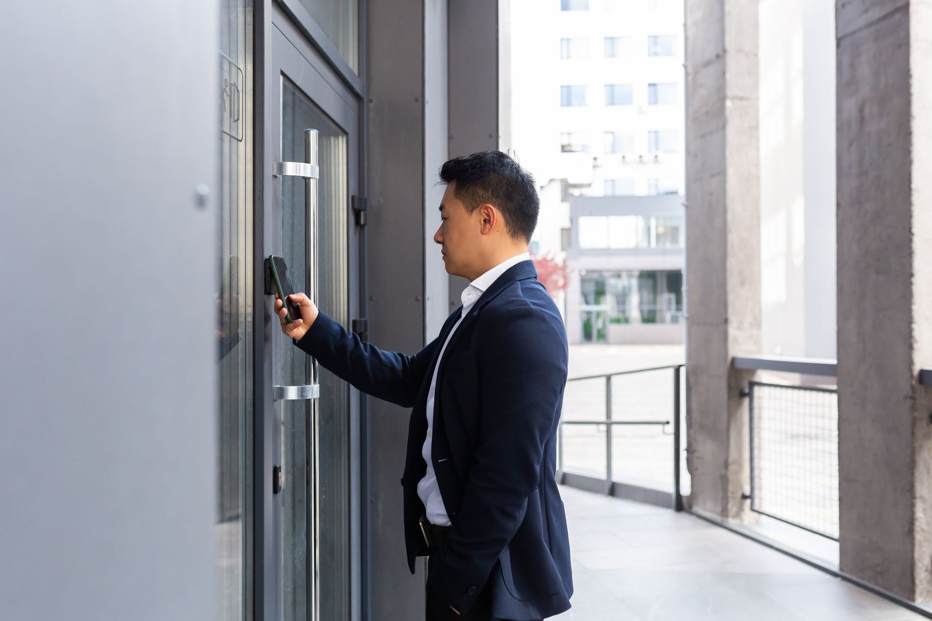 Man in suit using keycard on a building access control system near an exterior entrance.