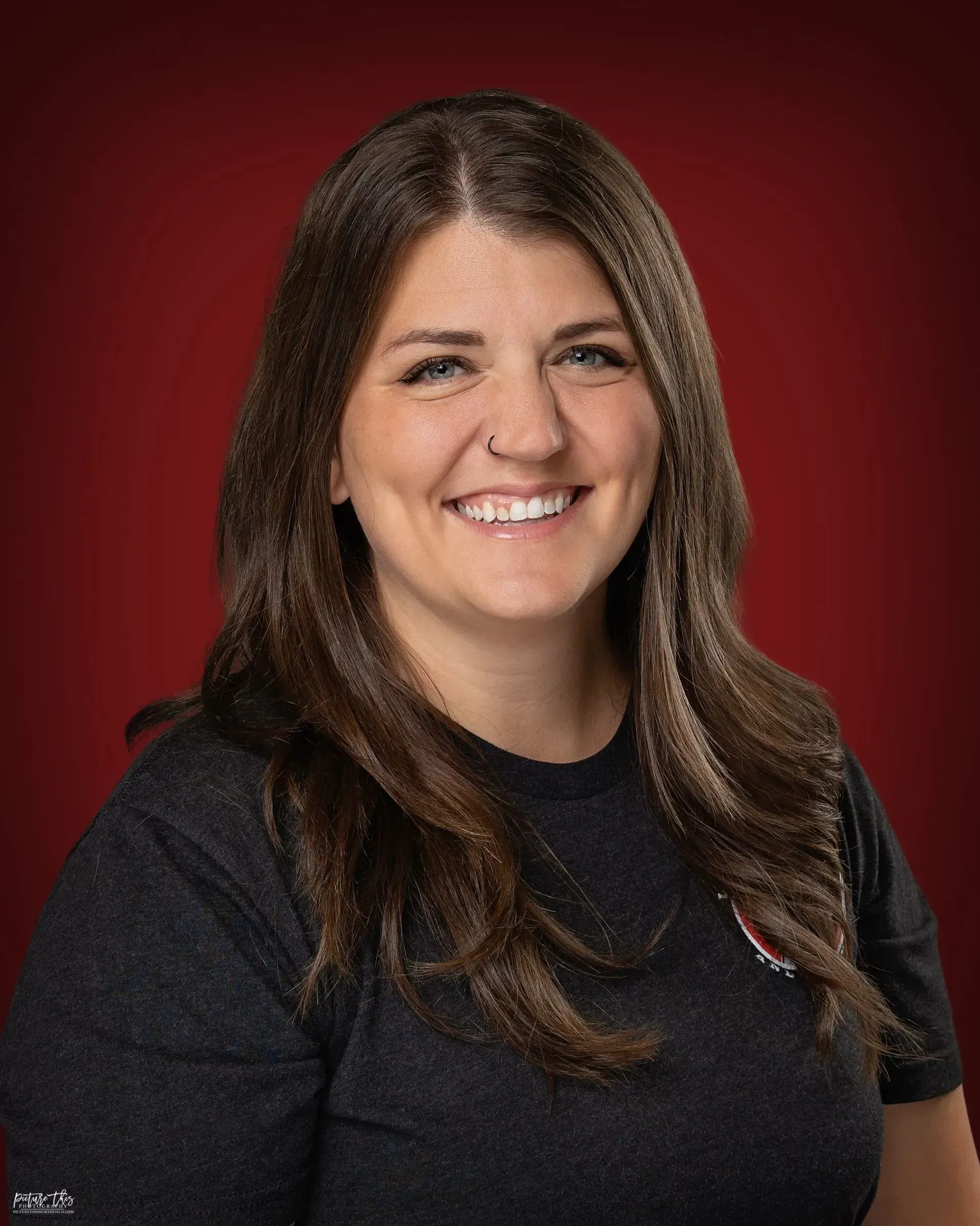 A woman in a black shirt is smiling in front of a red background.