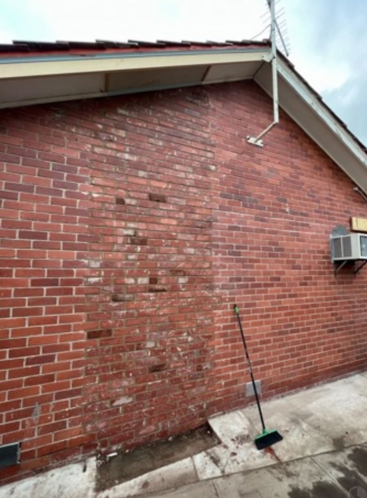 Red brick building exterior with missing bricks and a broom propped against the wall.