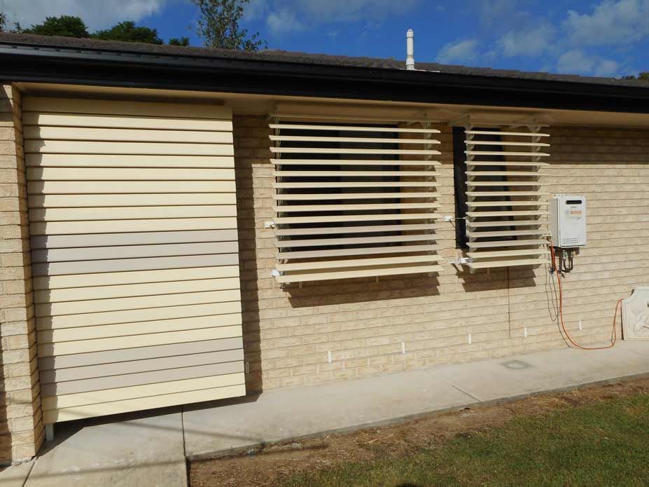 Beige Louvered Shutters Covering Windows on a Brick Building — Toowoomba Shade & Canvas in Harristown, QLD