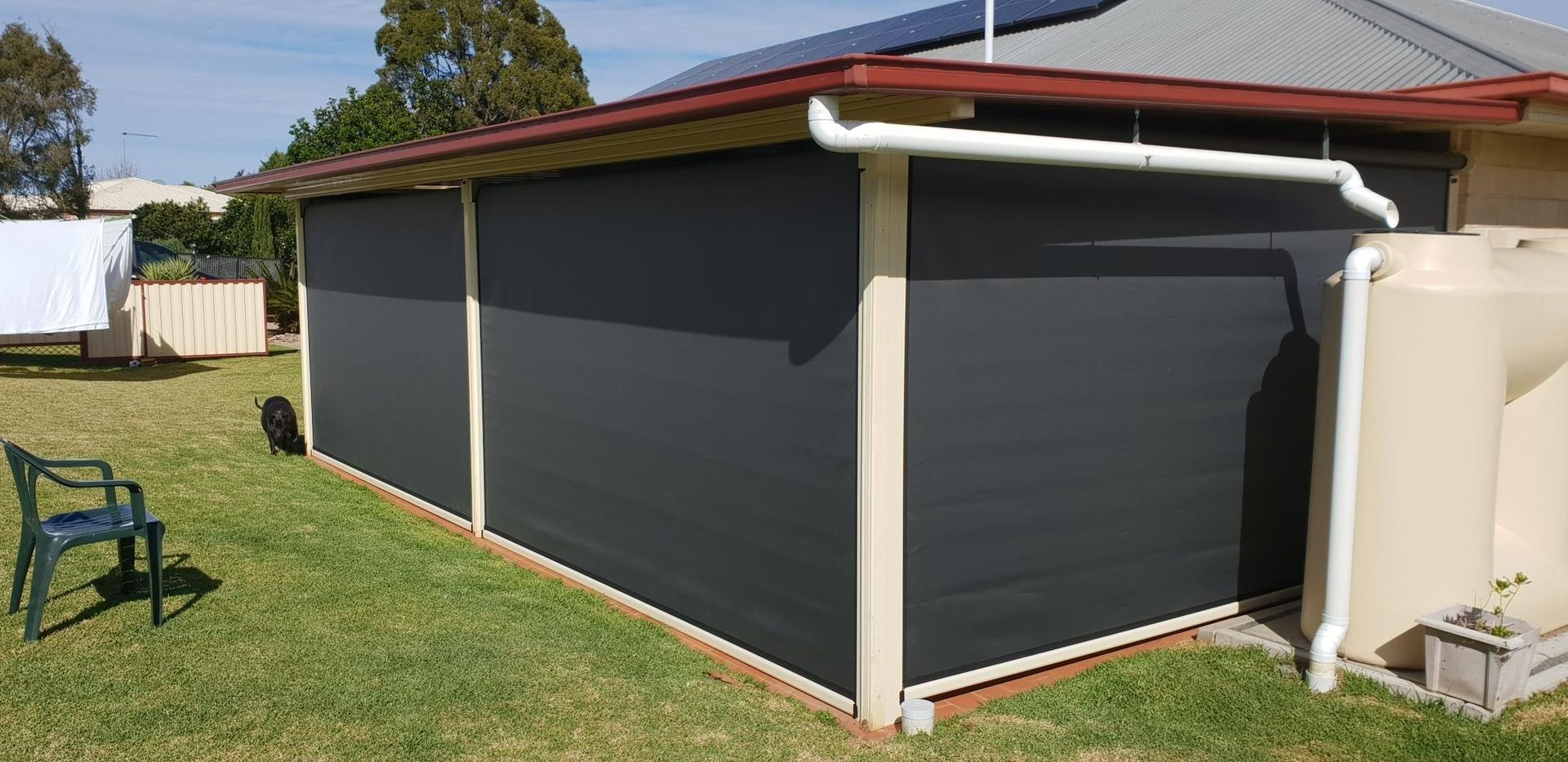 Dark Outdoor Blinds on a Building With a Rainwater Tank and Green Grass — Toowoomba Shade & Canvas in Harristown, QLD