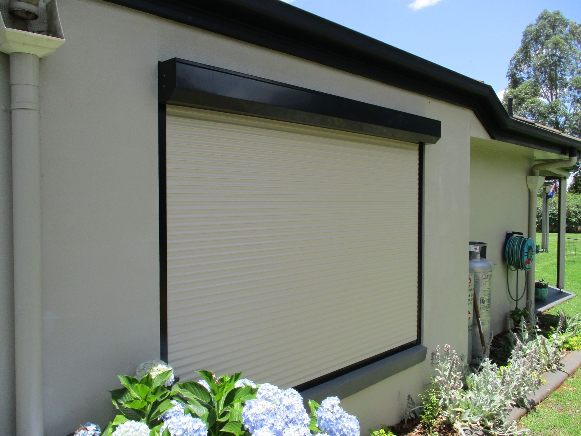 Exterior of a House With a Closed Beige Roller Shutter Over a Window — Toowoomba Shade & Canvas in Plainlands, QLD