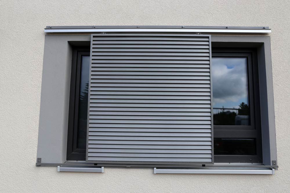 Gray Horizontal Louvered Window Shutter Partially Covering a Window — Toowoomba Shade & Canvas in Harristown, QLD
