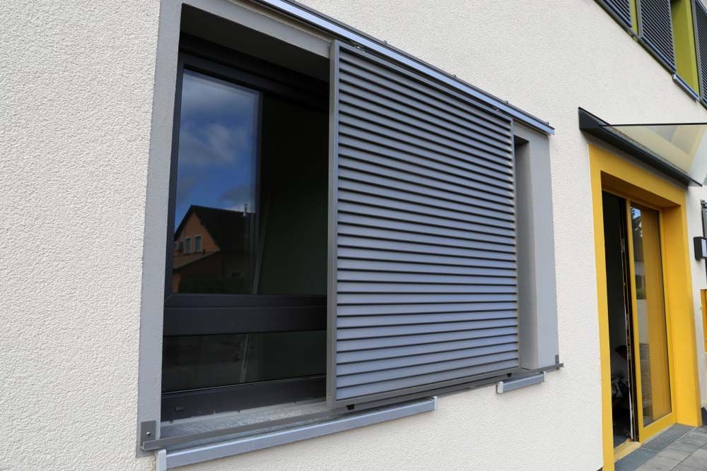 Window With Gray Sliding Louvered Shutter, Reflecting a Building — Toowoomba Shade & Canvas in Harristown, QLD
