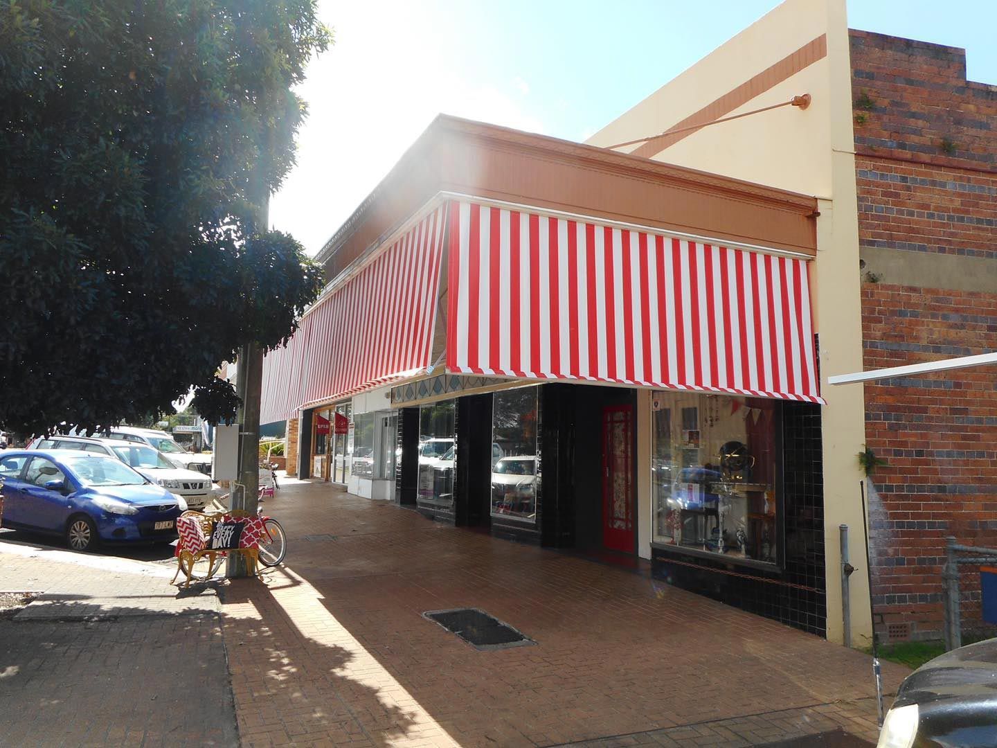Storefront with red and white striped awning, sidewalk, and parked cars.