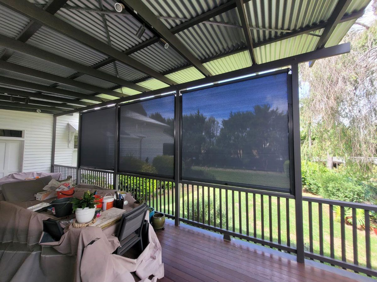 Porch with black sun shades, brown deck, green railing, and corrugated roof.