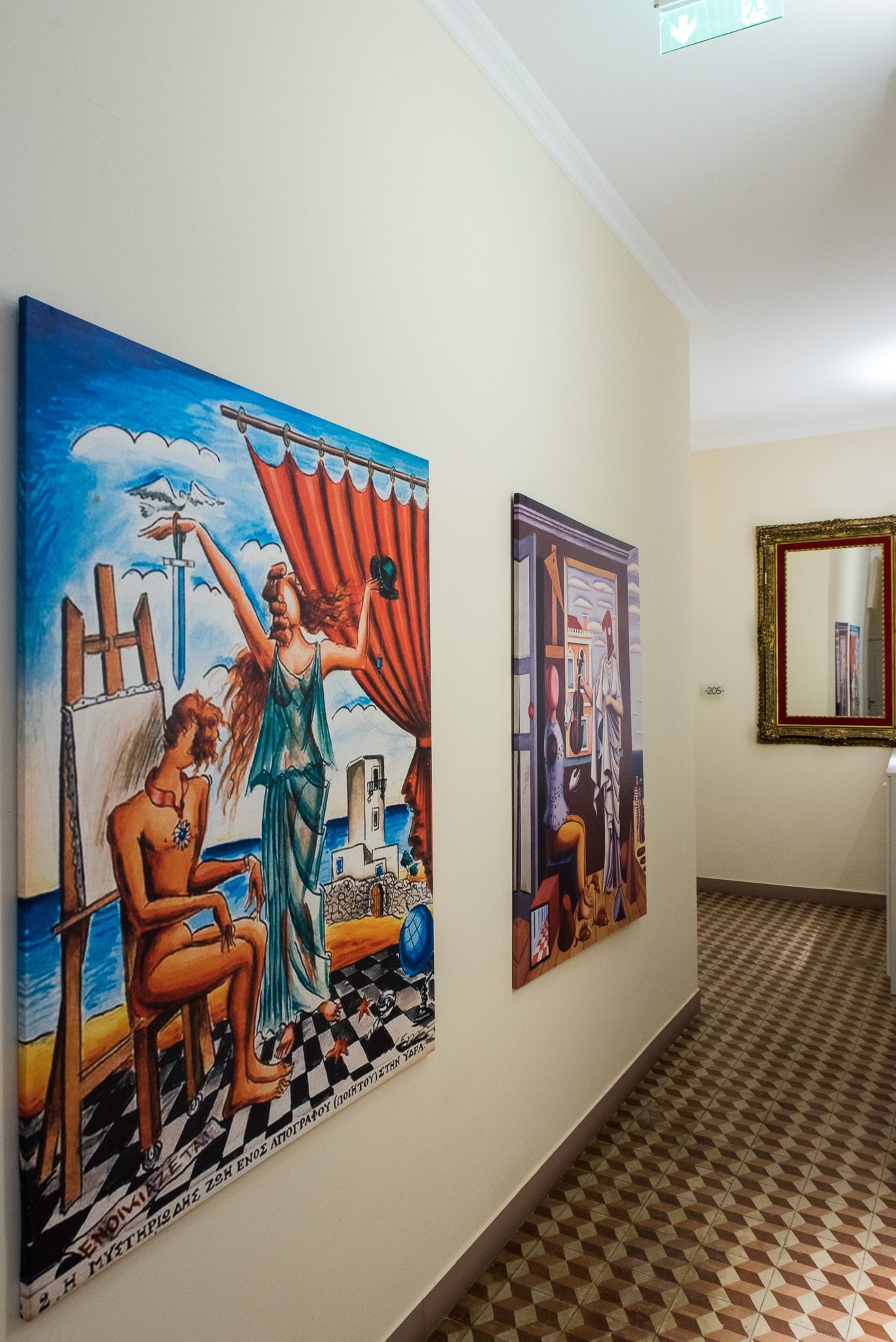 Δύο πίνακες σε κορνίζα κρέμονται σε έναν κρεμ τοίχο του διαδρόμου που οδηγεί σε έναν καθρέφτη στο τέλος ενός διαδρόμου με σχέδια από πλακάκια.