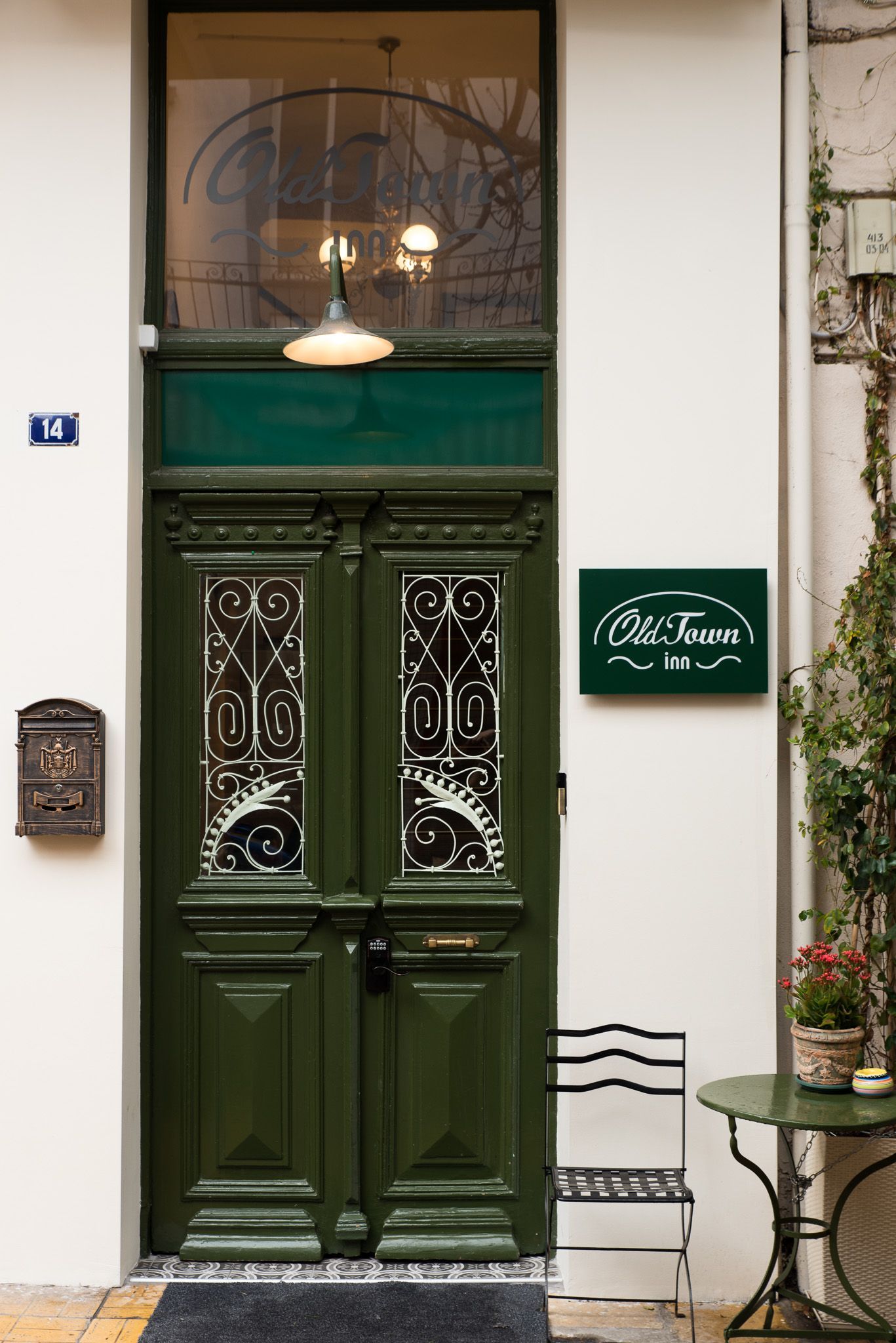 Μια σκούρα πράσινη διπλή πόρτα με περίτεχνα γυάλινα πάνελ, μια ασορτί πινακίδα που έγραφε «Olle Frans Inn» και ένα μικρό τραπεζάκι καφέ εκεί κοντά.