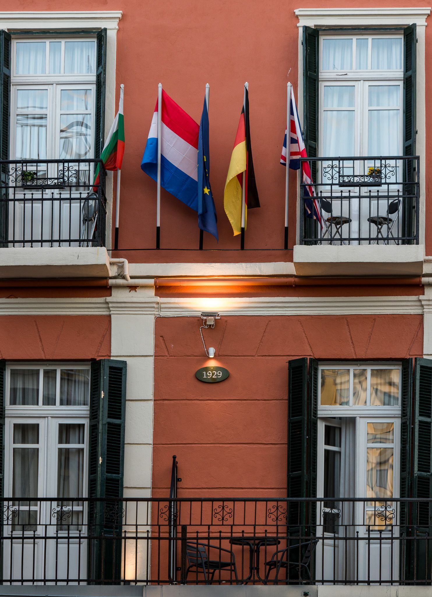 Ένα κτίριο σε σομόν χρώμα στο εξωτερικό του με δύο μπαλκόνια, στο οποίο κρέμονται αρκετές ευρωπαϊκές σημαίες ανάμεσα στα πάνω παράθυρα.
