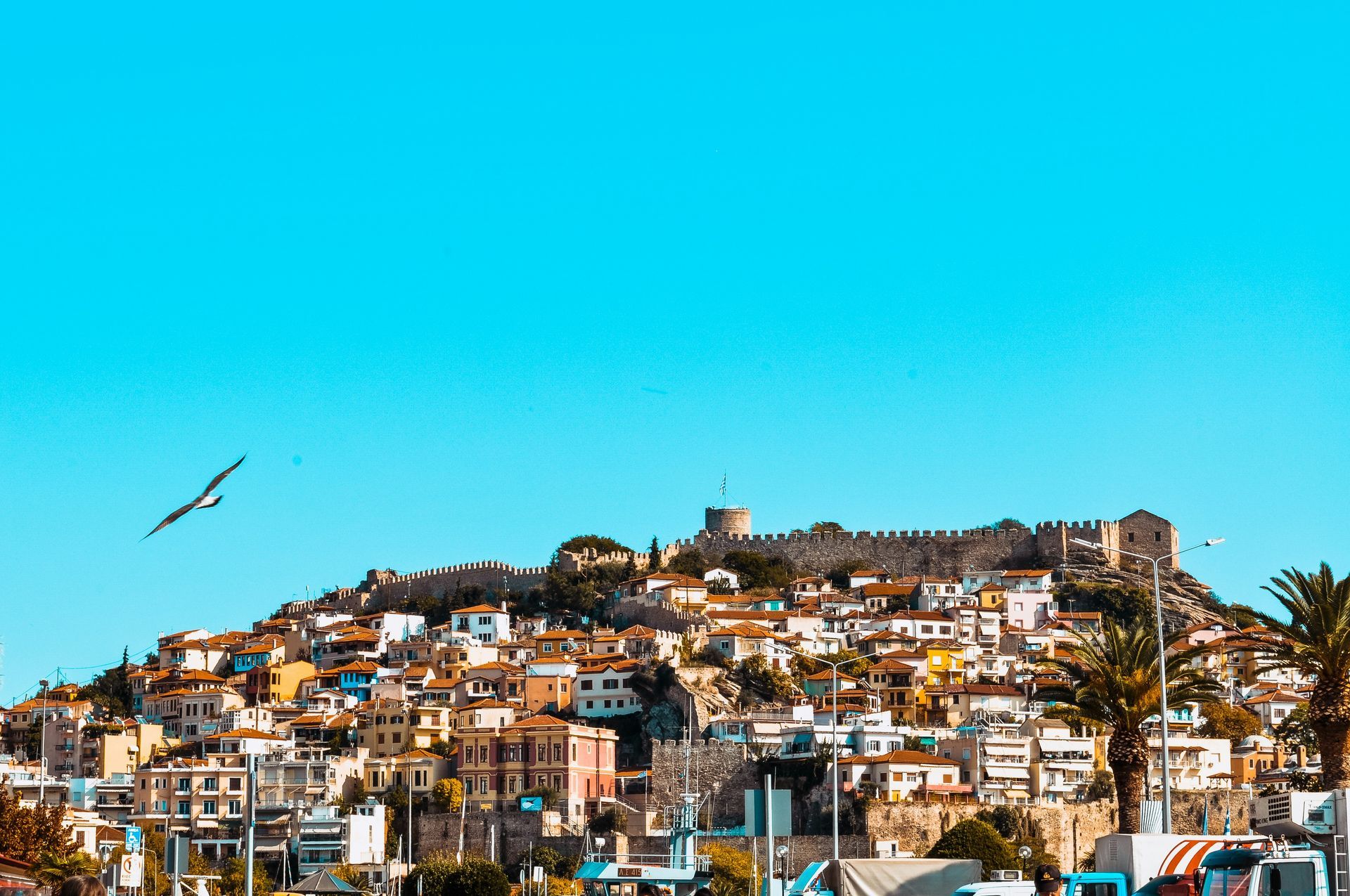 A hillside town with clustered buildings topped by an old stone fortress under a bright, cloudless blue sky.
