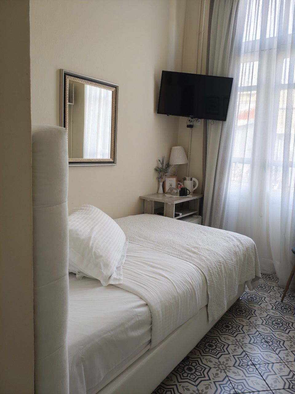 A small hotel room with a single white bed, a mirror on the wall, a nightstand, and a TV.