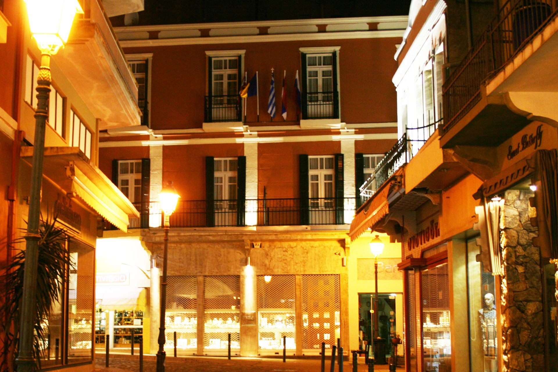 Μια θέα από το επίπεδο του δρόμου ενός κτιρίου στο χρώμα της σκουριάς τη νύχτα, φωτισμένου από ζεστές λάμπες του δρόμου σε μια πλατεία πόλης ευρωπαϊκού στιλ.