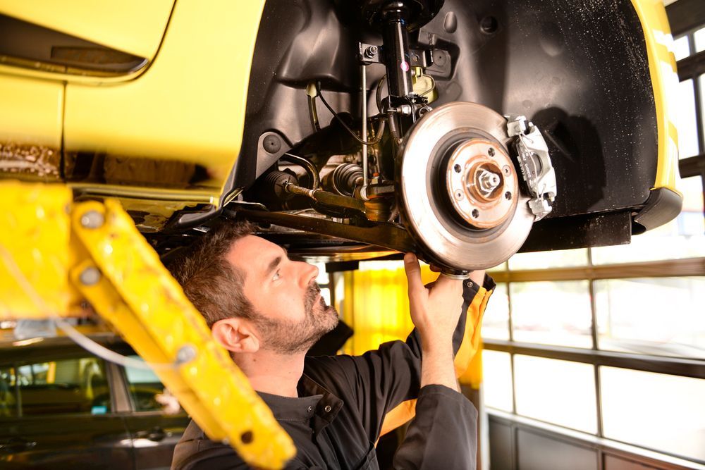 A Man Is Working On A Yellow Car In A Garage — Dunhams Auto Repairs In Woonona, NSW