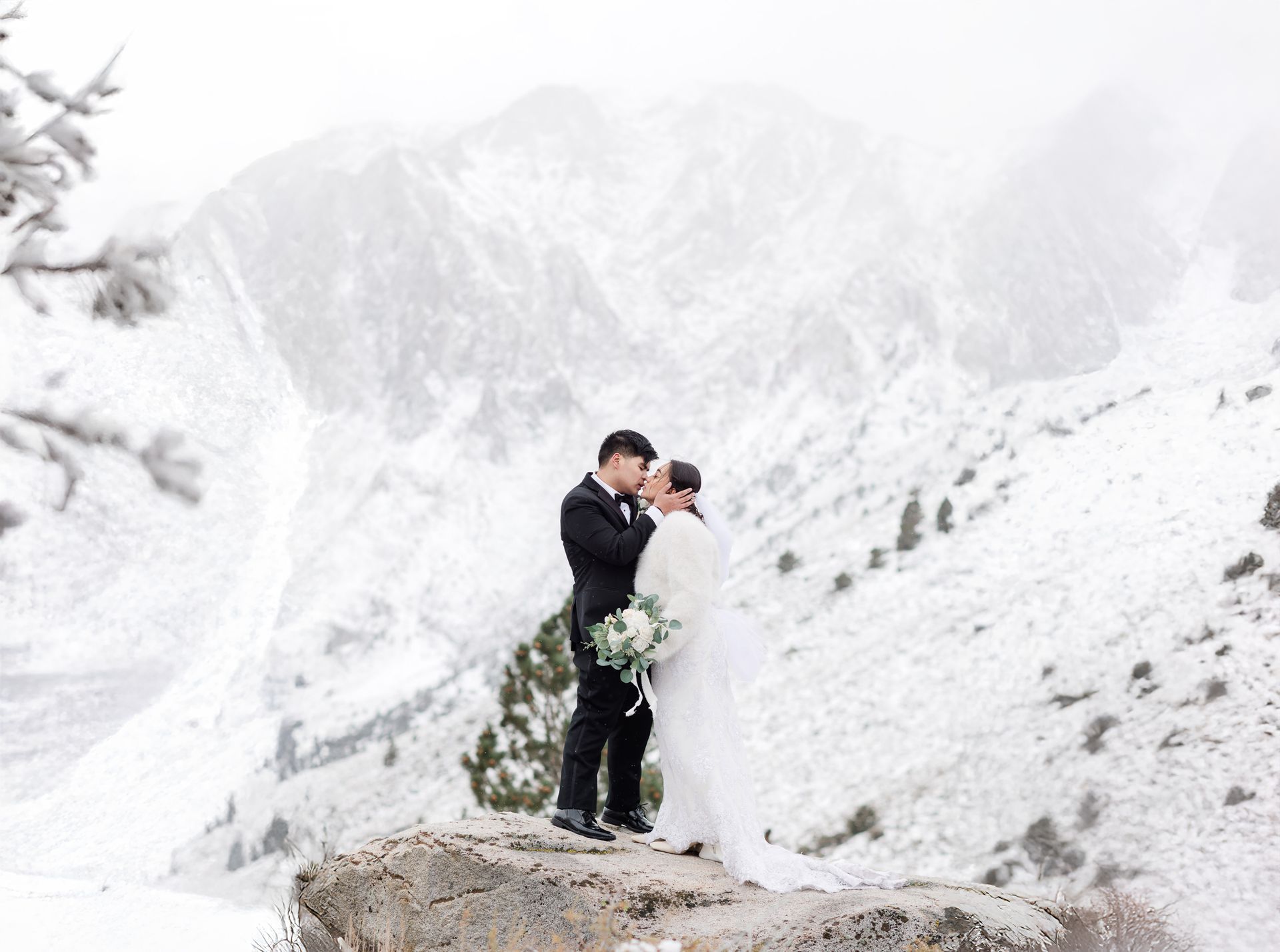 A bride and groom are walking through the snow holding hands.