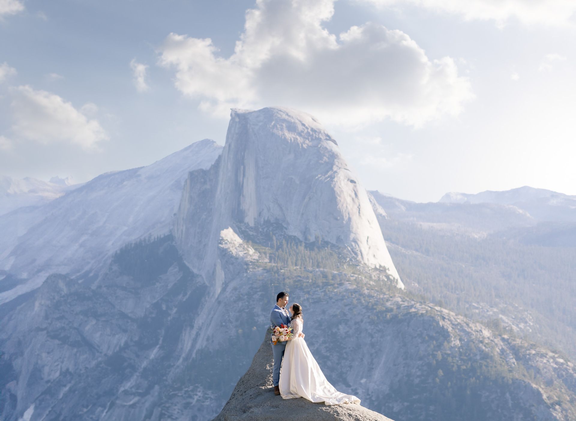 a bride and groom are kissing on top of a mountain at yosemite national park