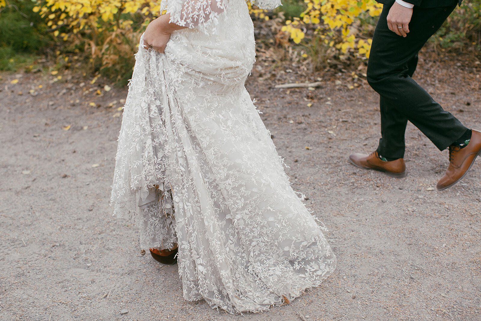 A bride and groom are walking down a dirt road.