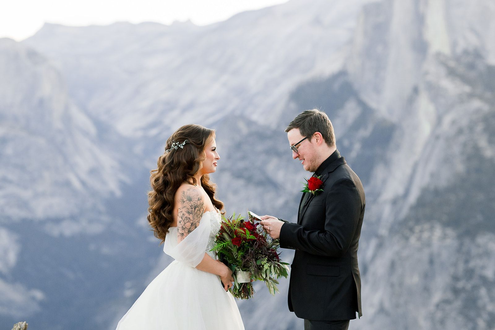 A bride and groom are standing next to each other in front of a mountain.