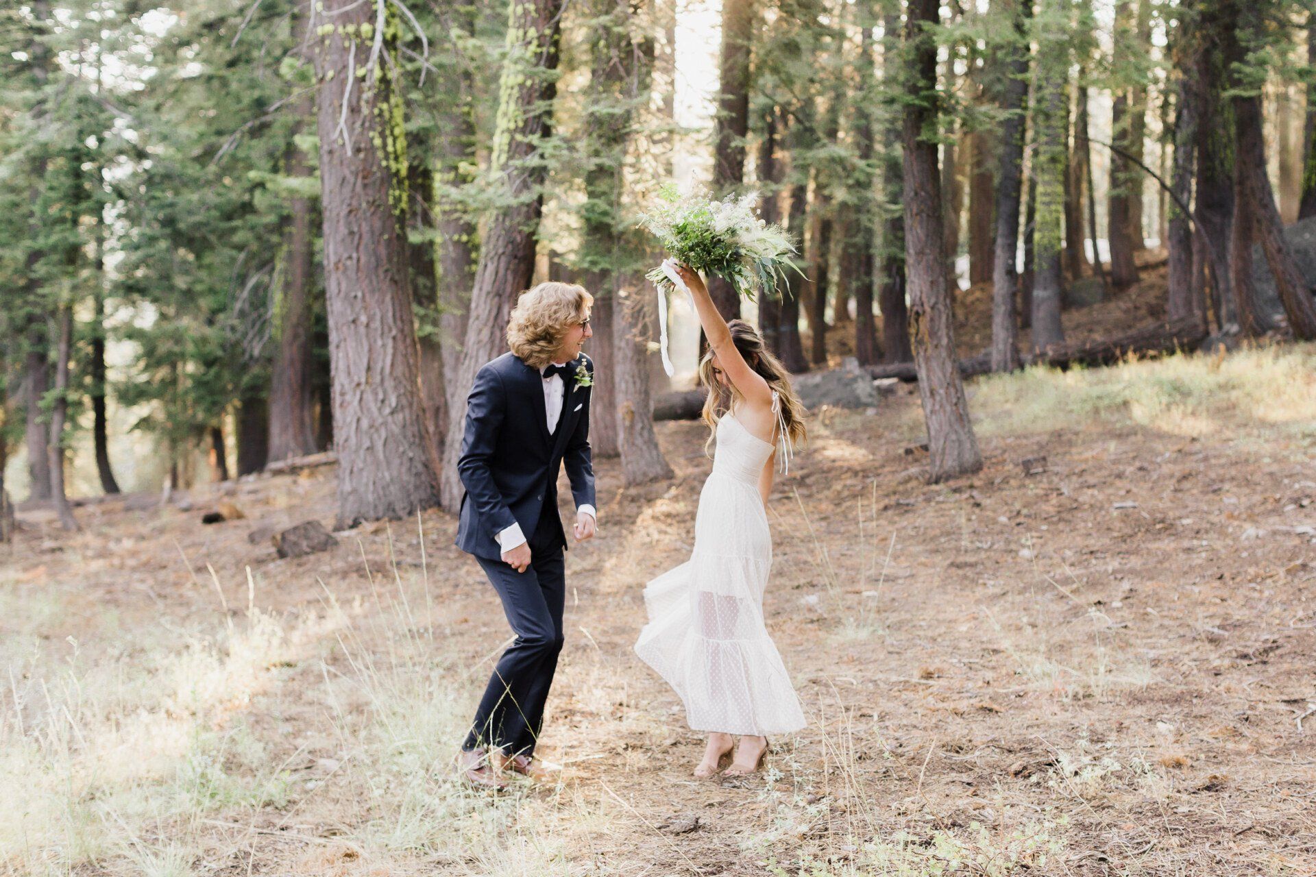 A bride and groom are dancing in the woods.