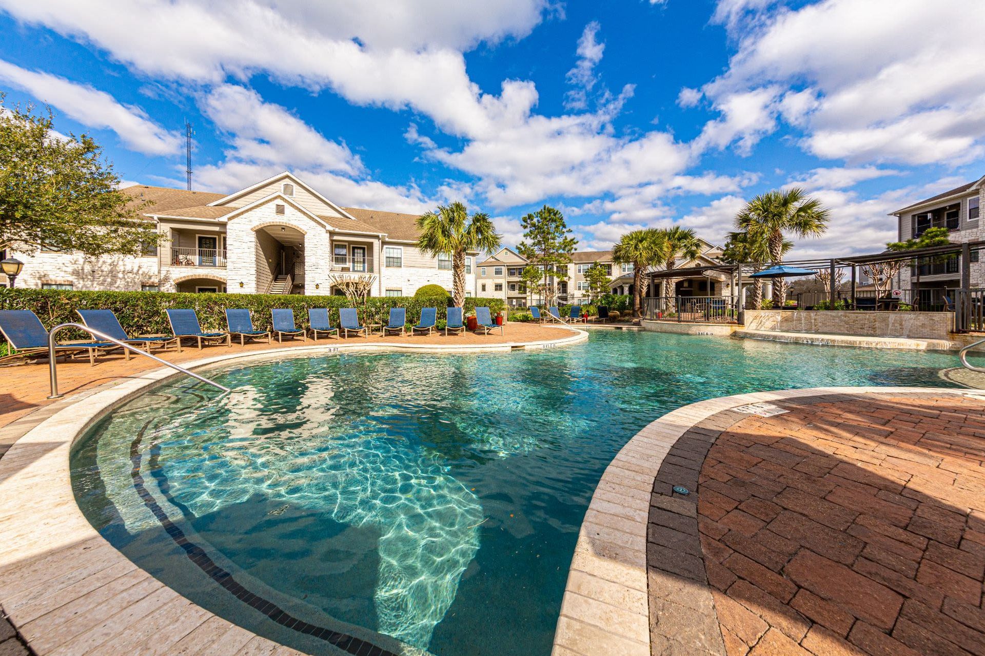 A large swimming pool in front of a building with chairs around it at Marquis Grand Lakes in Richmond, TX.