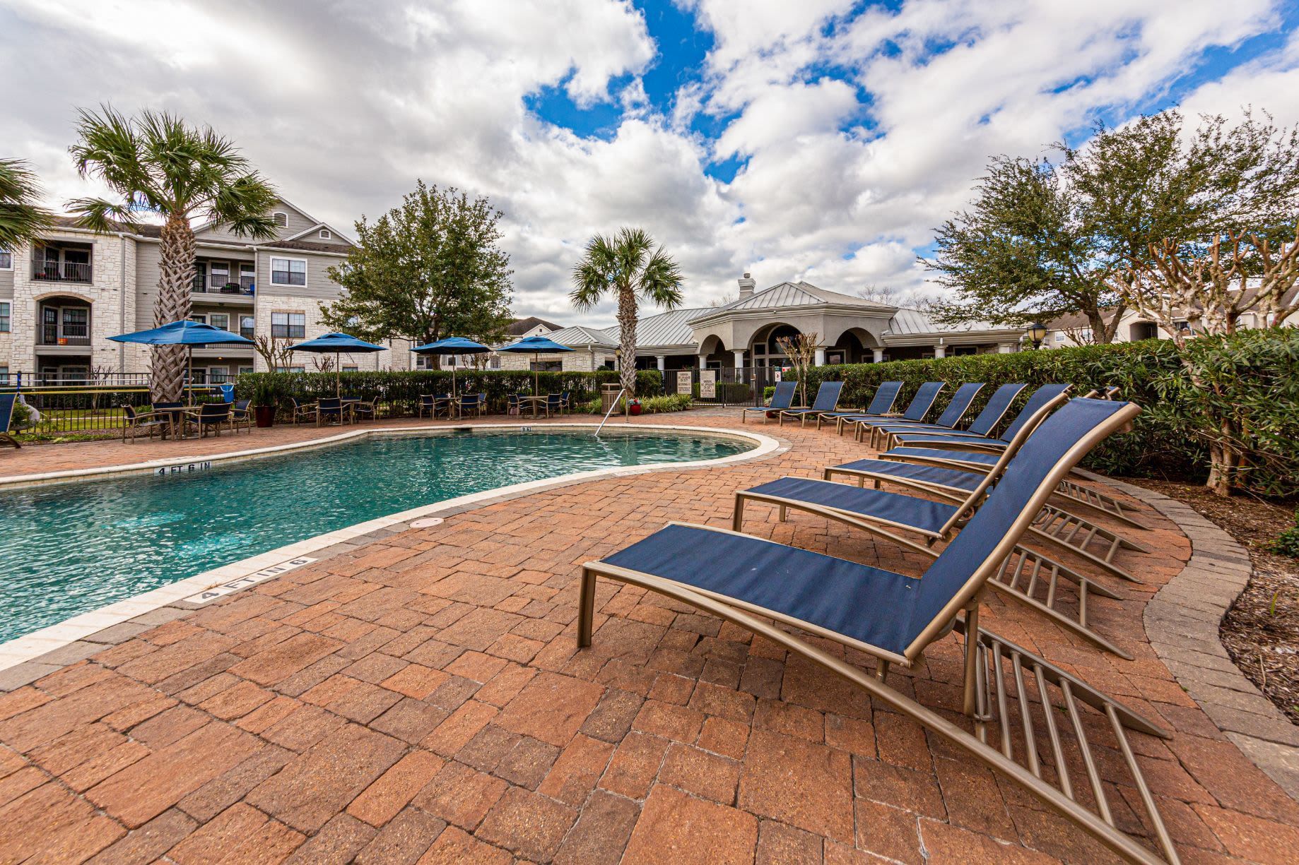 A row of lounge chairs is sitting next to a large swimming pool at Marquis Grand Lakes in Richmond, TX.
