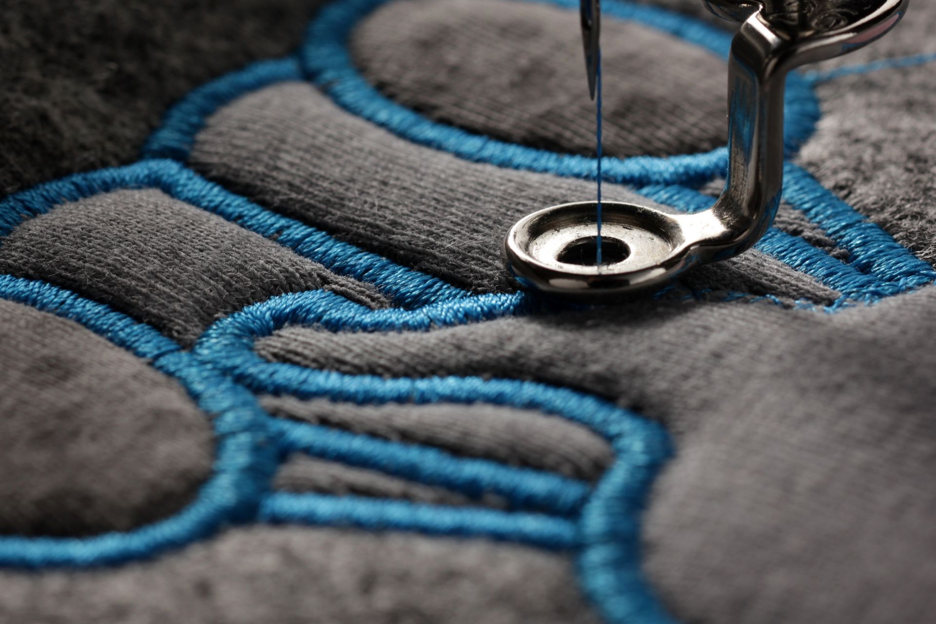 Close-up of embroidery machine stitching blue thread onto gray fabric, creating a design.