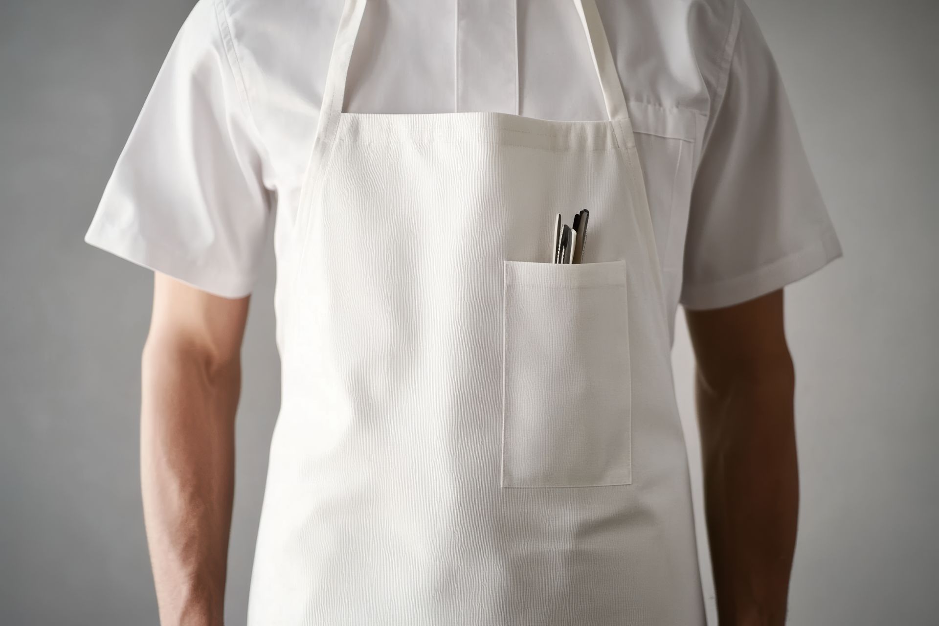 Chef wearing white apron and shirt, two pens in apron pocket.