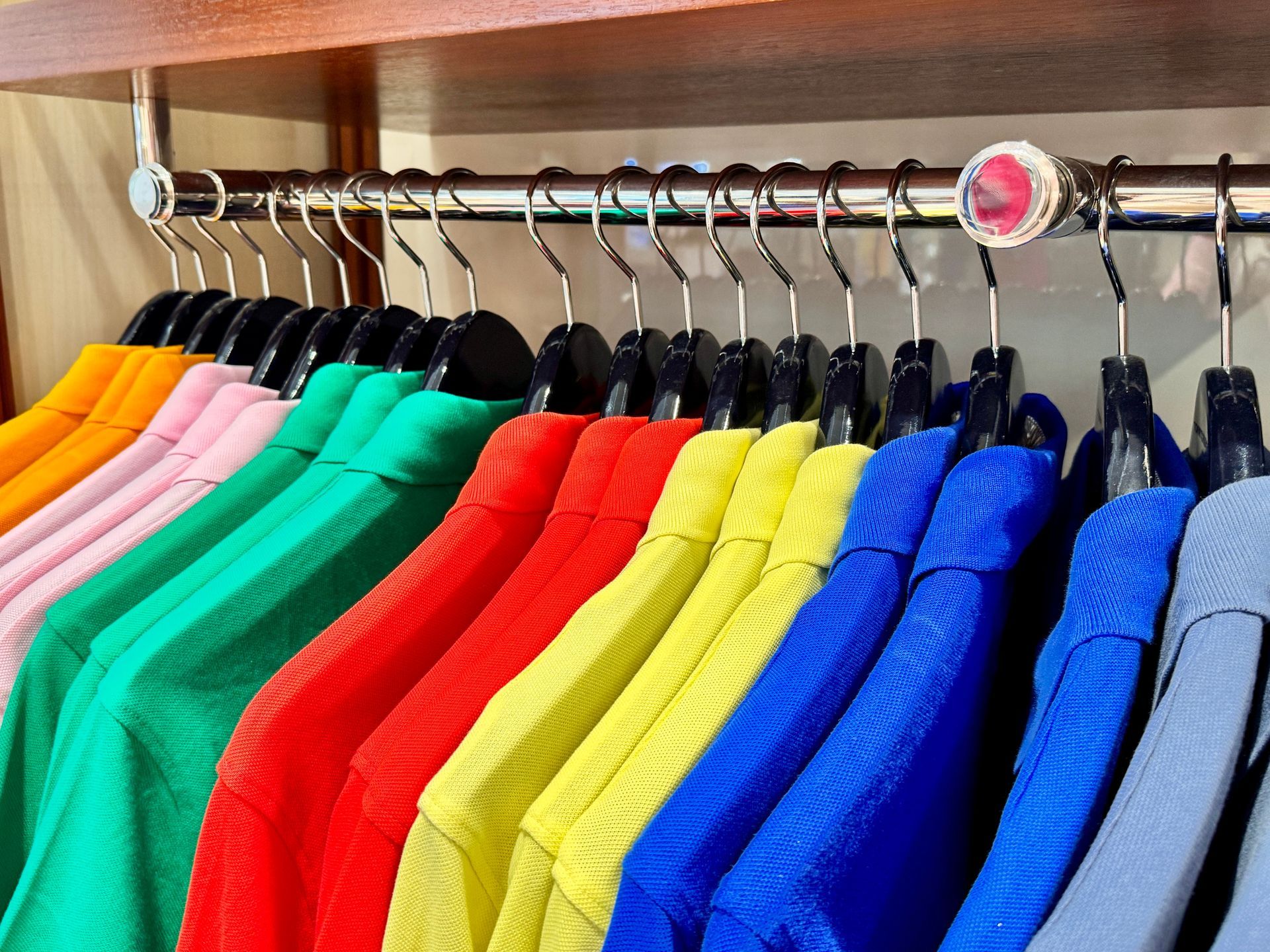 Row of colorful shirts hanging on a rack inside a closet.