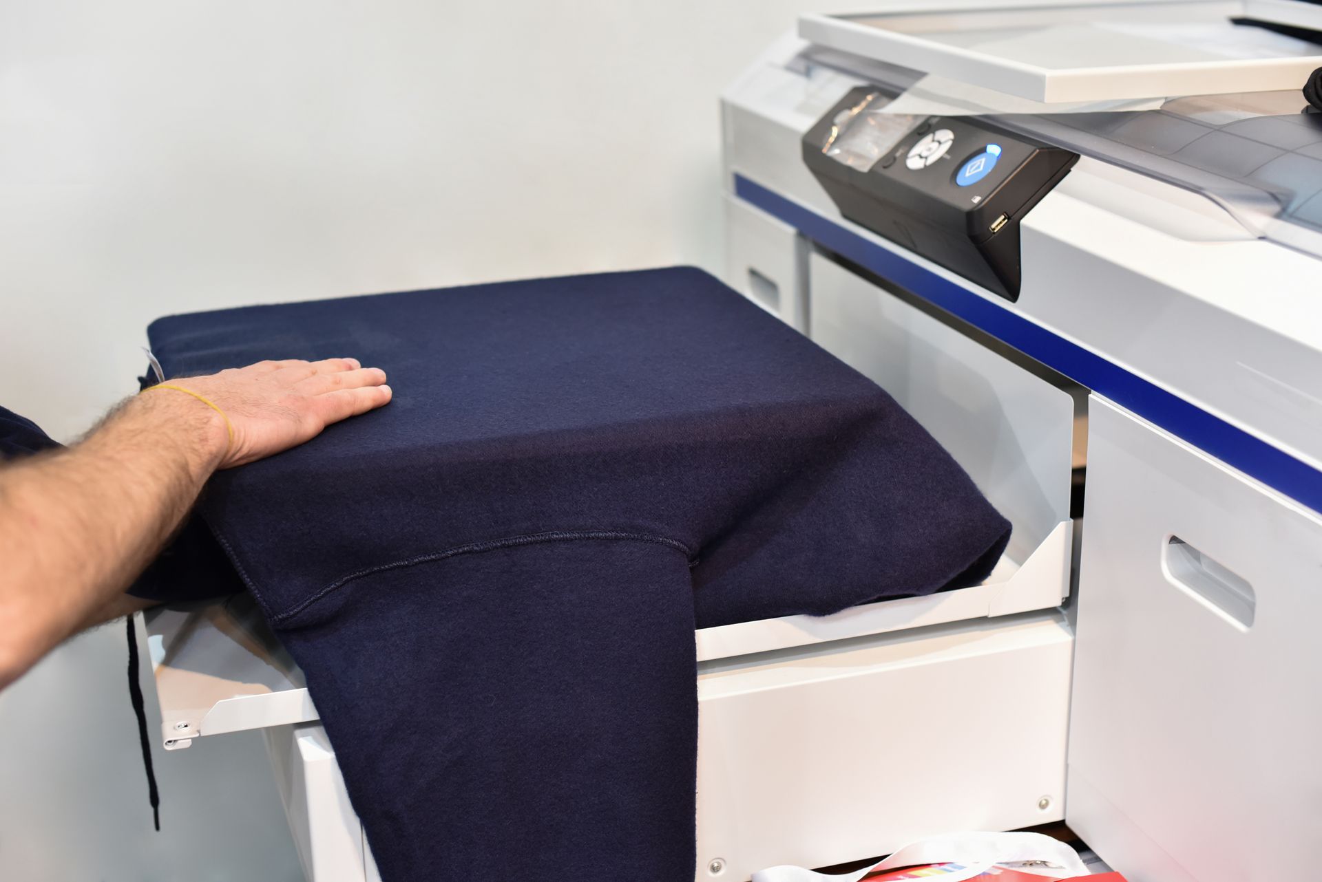 Person placing dark blue fabric on a white machine; fabric partially covering the machine.