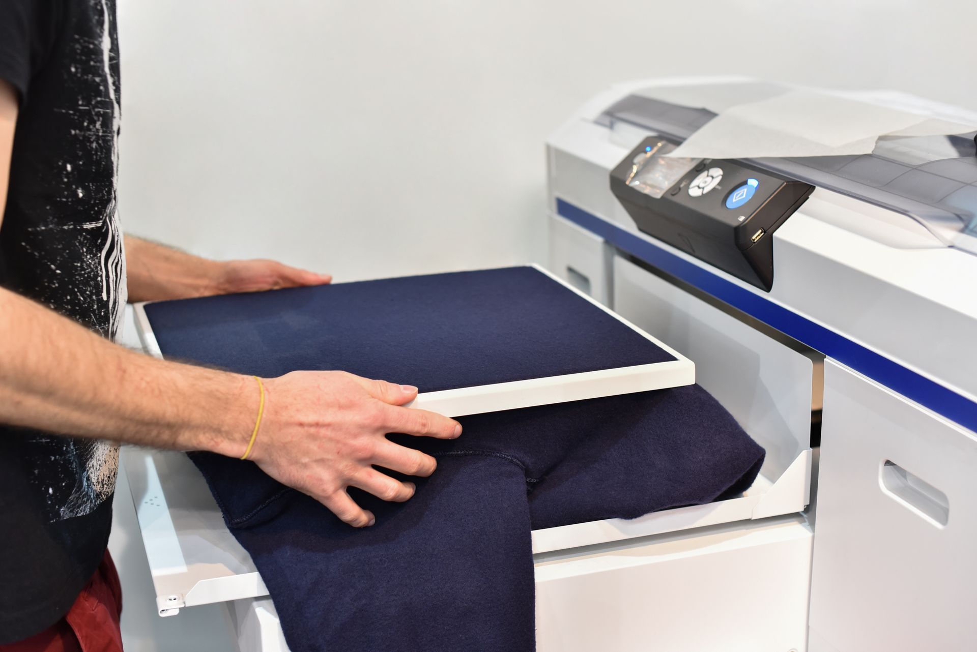 Person placing dark fabric on a printing machine's bed. The machine is white with blue accents.