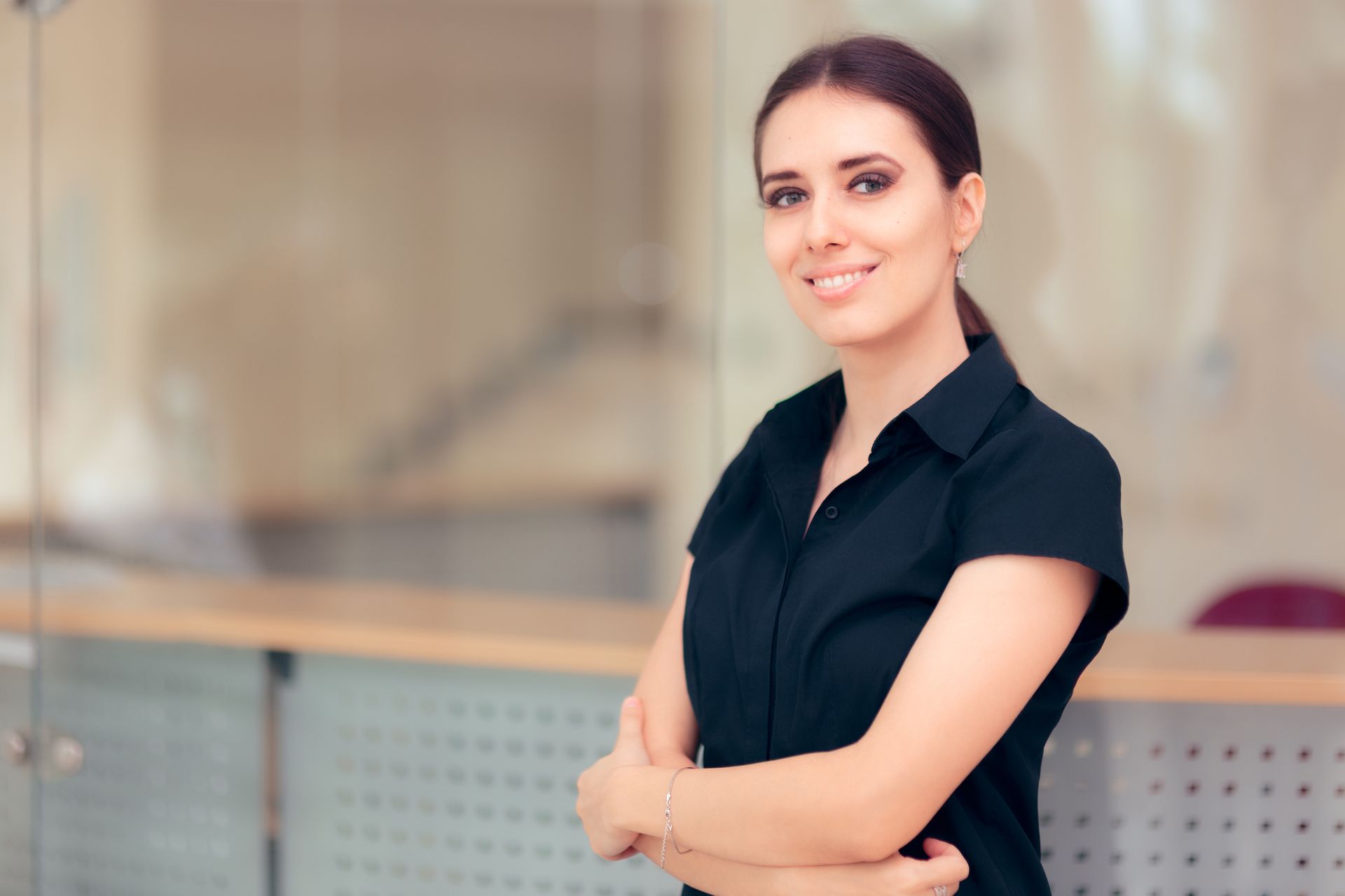 Woman in black shirt, arms crossed, smiling in an office setting.
